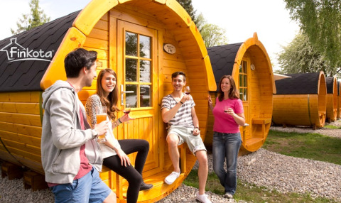 Quatre jeunes adultes apprécient le glamping devant des cabanes en bois en forme de tonneau au Camping Rissbach - Wijnvaten Rijnland-Palts.