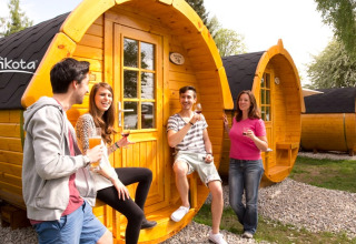 Vier jonge mensen genieten van glamping bij houten wijnvaten op Camping Rissbach - Wijnvaten Rijnland-Palts.