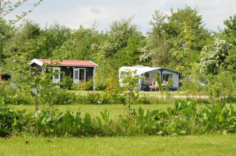 Two people relaxing outside a caravan and tiny house in lush greenery at Parkcamping de Graafschap, Gelderland.