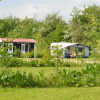 Two people relaxing outside a caravan and tiny house in lush greenery at Parkcamping de Graafschap, Gelderland.