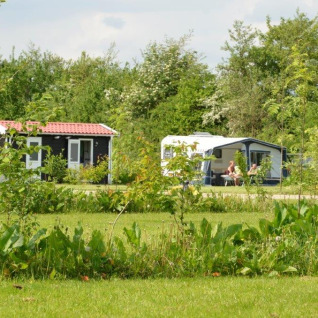 To personer slapper af foran en campingvogn og tiny house blandt grønne omgivelser på Parkcamping de Graafschap.