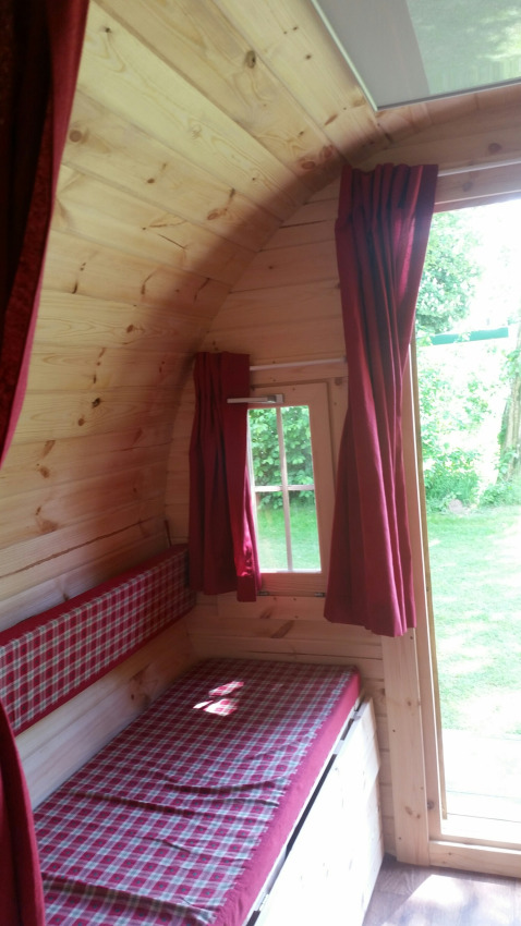 Intérieur d'une cabane glamping avec murs en bois, lit à carreaux et rideaux rouges à Gelderland.