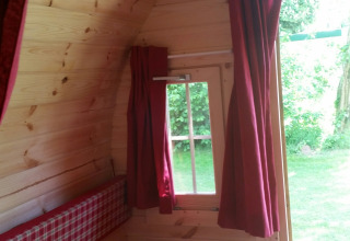 Indvendig af glampinghytte med træpaneler, ternet seng og røde gardiner på Parkcamping de Graafschap.