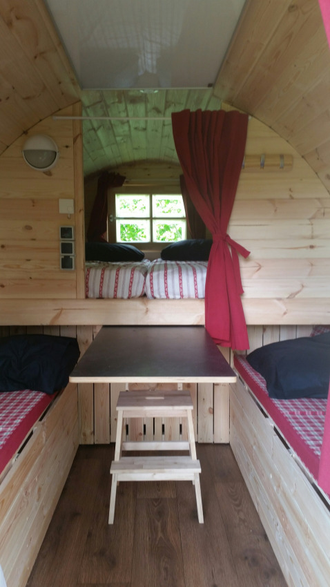 Interior de alojamiento glamping de madera en Parkcamping de Graafschap con camas, cortinas y mesa.