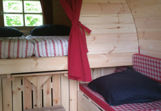Glampingaccommodatie met houten interieur, stapelbed en rode gordijnen bij Parkcamping de Graafschap.