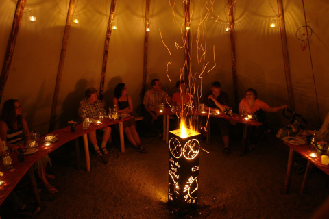 Vue intérieure d’un tipi avec des gens assis autour d’un feu décoratif au Camping Gieselwerder.