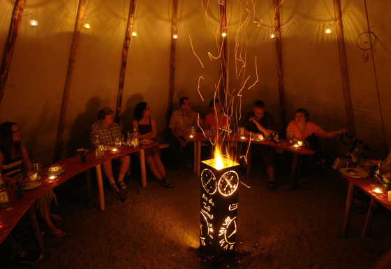 Binnenaanzicht van een tipi waar mensen rond een decoratief vuur zitten bij Camping Gieselwerder.