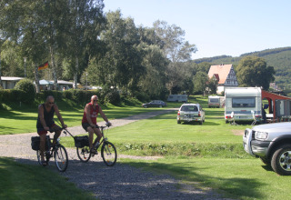 To mænd cykler gennem en grøn campingplads med autocampere og telte på Camping Gieselwerder i Hessen.