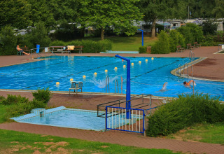Udendørs swimmingpool på Camping Gieselwerder med svømmere, liggestole og grønne omgivelser i Hessen.