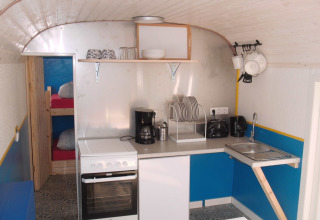 Køkkenområde i en glamping pipowagen med køjesenge, komfur, opvaskemaskine og køkkenredskaber i Hessen.