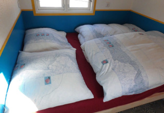 Vista interior de una cama acogedora con edredones dobles en alojamiento glamping en Camping Gieselwerder.