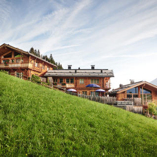 Chalets en bois du HochLeger Chalet Refugium - Chalet Tirol perchés sur une colline verdoyante face aux montagnes.