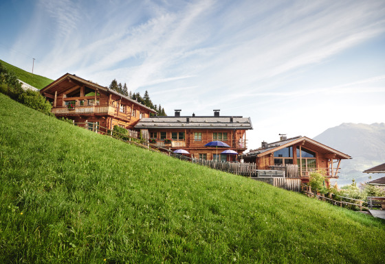 Chalets en bois du HochLeger Chalet Refugium - Chalet Tirol perchés sur une colline verdoyante face aux montagnes.