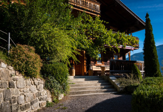 HochLeger Chalet Refugium - Chalet Tirol, luxuriöse Glamping-Unterkunft mit Garten und Holzveranda im Sonnenschein.