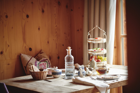Rustik morgenmad på træbord i HochLeger Chalet Refugium - Chalet Tirol, med frugt, brød og te ved vindue.