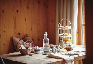 Rustik morgenmad på træbord i HochLeger Chalet Refugium - Chalet Tirol, med frugt, brød og te ved vindue.
