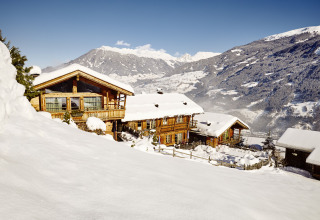 Alloggio glamping HochLeger Chalet Refugium - Chalet Tirol in inverno, chalet in legno e montagne innevate sullo sfondo.