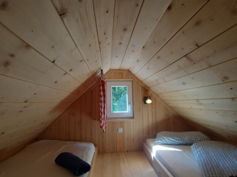 Vista interna di un'accogliente tenda glamping con pannelli in legno, due letti singoli e una piccola finestra.