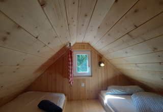 Innenansicht einer gemütlichen Glamping-Lodge mit Holzverkleidung, zwei Einzelbetten und kleinem Fenster.