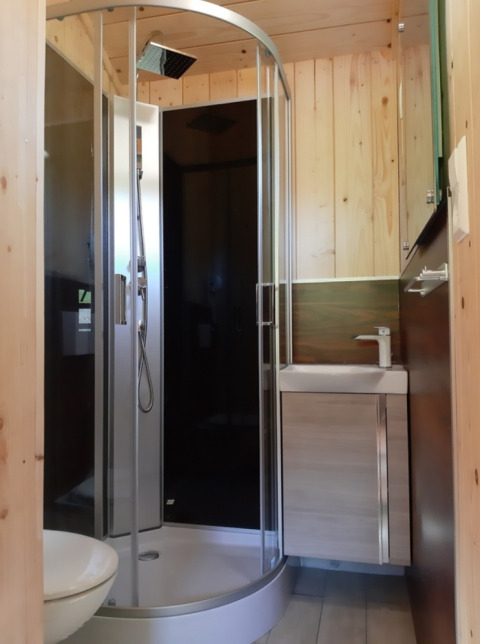 Bagno moderno con doccia curva in vetro e pannelli di legno in una glamping lodge nella Foresta Nera, Germania.