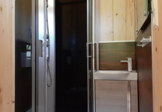 Salle de bain moderne avec douche arrondie et panneaux en bois dans un lodge de glamping en Forêt-Noire, Allemagne.