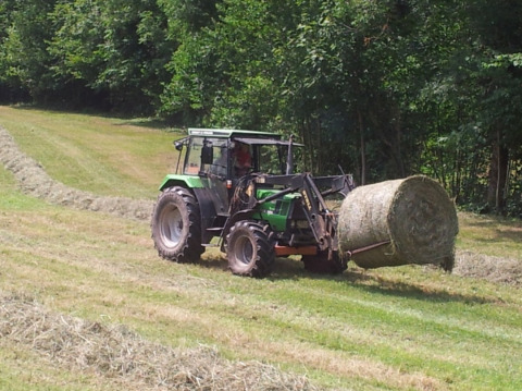 Un trattore solleva una grande balla di fieno vicino ai lodge Boerderij Gallushof nella Foresta Nera, Germania.