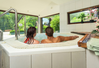 Paar entspannt gemeinsam im Innenwhirlpool mit Blick auf grüne Natur in den Glamping Vogezen Chalets.
