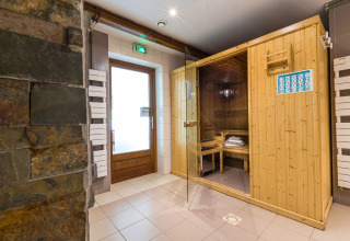 Zona de spa interior con sauna de madera y pared de piedra en Auberge et Chalets de la Wormsa - Glamping Vogezen.