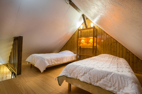 Chambre mansardée chaleureuse avec deux lits simples et murs en bois, glamping Auberge et Chalets de la Wormsa.