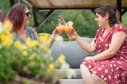 Dos mujeres brindan con cócteles al aire libre en Auberge et Chalets de la Wormsa - Glamping Vogezen, rodeadas de flores.