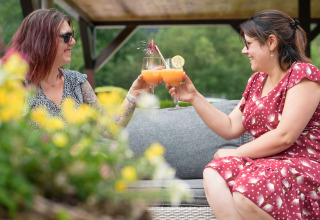 Due donne brindano all'aperto con cocktail presso Auberge et Chalets de la Wormsa - Glamping Vogezen, circondate da fiori.