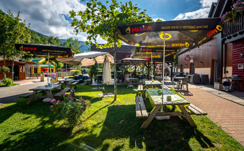 Udendørs spiseplads med træborde og store parasoller på Auberge et Chalets de la Wormsa Glamping Vogezen.