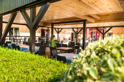 Überdachte Terrasse im Auberge et Chalets de la Wormsa Glamping Vogezen mit Tischen, Stühlen und Holzdach.