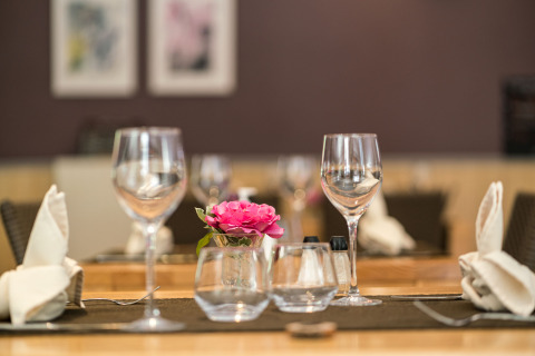 Mesa elegantemente puesta en Auberge et Chalets de la Wormsa - Glamping Vogezen, con copas y flor rosa.