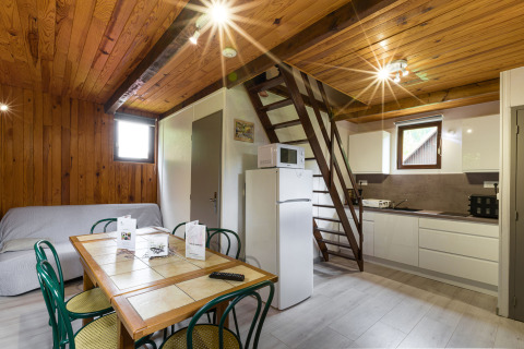 Interior de cabaña de madera con cocina, mesa de comedor, escalera de altillo y sofá, Auberge et Chalets de la Wormsa, Glamping Vogezen.