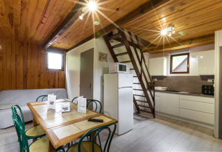 Innenraum einer Holzhütte mit Küche, Esstisch, Schlafboden und Sofa, Auberge et Chalets de la Wormsa, Glamping Vogezen.