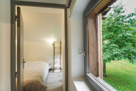 Udsigt til et soveværelse med dobbeltseng og åbent vindue, der viser grønne træer i Glamping Vogezen.