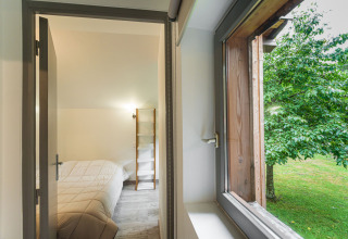 Vista su una camera da letto con letto matrimoniale e finestra aperta su alberi verdi a Glamping Vogezen.