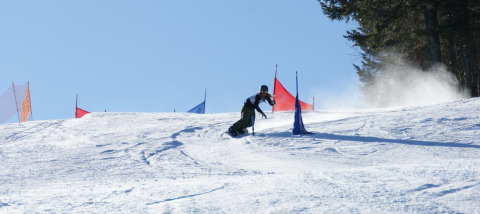 Skiløber suser ned ad en piste med flag i Auberge et Chalets de la Wormsa - Glamping Vogezen, under blå himmel.