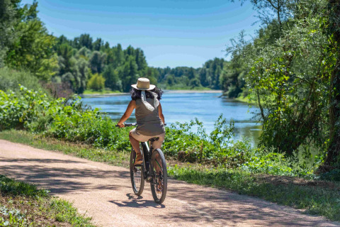 Frau fährt bei sonnigem Wetter mit dem Fahrrad am Fluss bei Domaine la Chabanne - Safaritenten Auvergne-Rhône-Alpes.