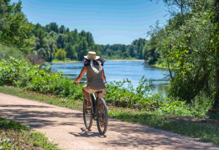 Vrouw fietst langs een rivier bij Domaine la Chabanne - Safaritenten Auvergne-Rhône-Alpes op een zonnige dag.