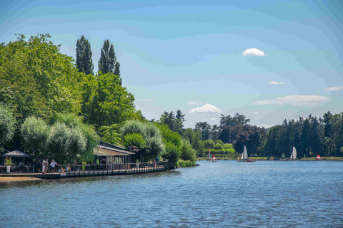 View of the lake at Domaine la Chabanne - Safaritenten Auvergne-Rhône-Alpes with sailboats and lush green trees.