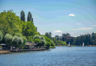 View of the lake at Domaine la Chabanne - Safaritenten Auvergne-Rhône-Alpes with sailboats and lush green trees.