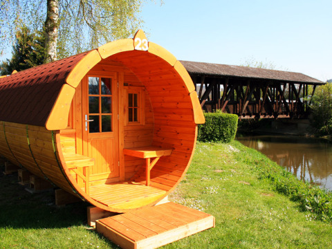 Hébergement glamping en fût en bois près de la rivière et d’un pont couvert à Camping Naturama Beilngries.