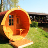 Barrel-shaped glamping cabin by the river at Camping Naturama Beilngries with a covered wooden bridge view.