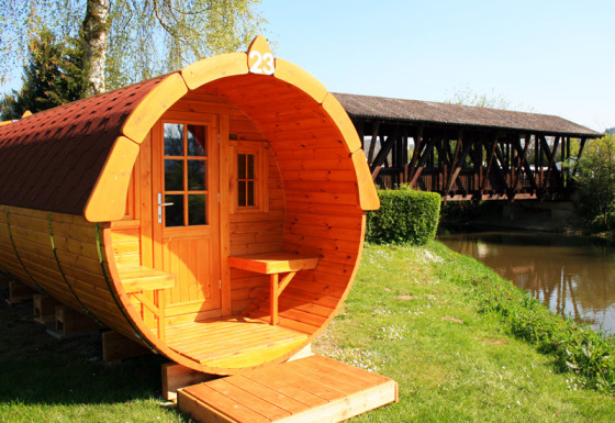 Hébergement glamping en fût en bois près de la rivière et d’un pont couvert à Camping Naturama Beilngries.