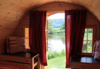 Indvendigt udsigt over glamping campinghytte med røde gardiner og udsigt til sø, Camping Naturama Beilngries.