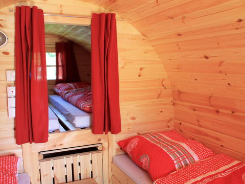Vue intérieure d’une cabane en bois confortable avec rideaux et literie rouges, camping glamping.
