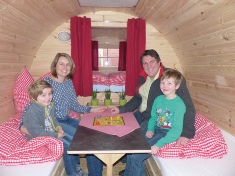 Familie nyder brætspil sammen i hyggelig glampingindkvartering med træsider og røde gardiner.