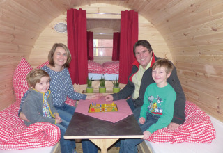 Gezin speelt een bordspel in een gezellige glamping accommodatie met houten wanden en rode gordijnen.